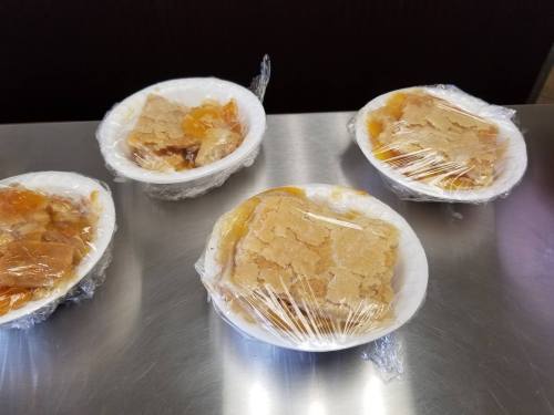 Four bowls of dessert covered with plastic wrap, sitting on a stainless steel surface.