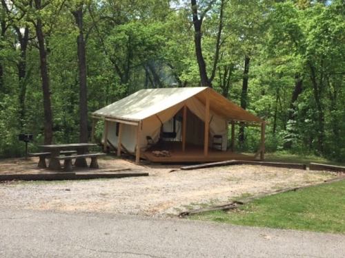 A canvas tent on a wooden deck surrounded by trees, with a picnic table nearby in a natural setting.