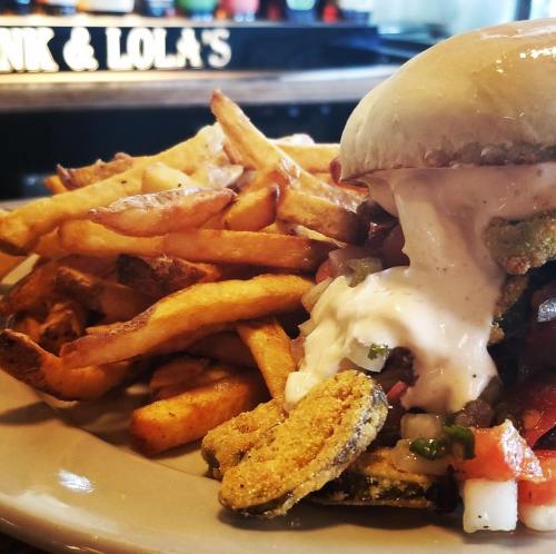 A close-up of a burger with sauce and toppings, served with a generous side of crispy French fries.