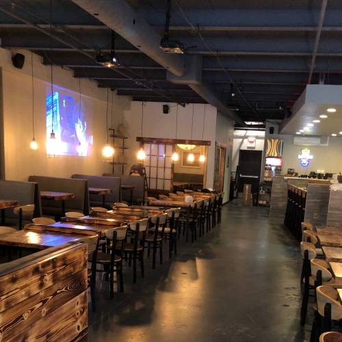 Interior of a restaurant with wooden tables, chairs, and a projector screen displaying an image on the wall.