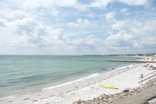 A serene beach scene with gentle waves, a sandy shore, and a yellow kayak on the sand under a partly cloudy sky.