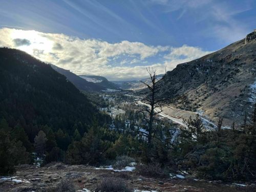 A scenic valley view with mountains, trees, and a winding river under a partly cloudy sky.