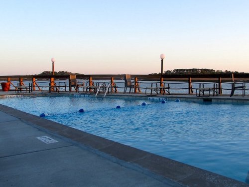 A serene poolside view at sunset, with chairs, pool floats, and a calm water backdrop.