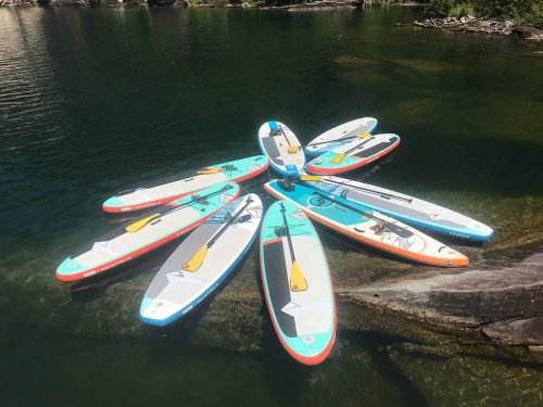 A cluster of colorful paddleboards arranged in a circular pattern on calm water, surrounded by greenery.