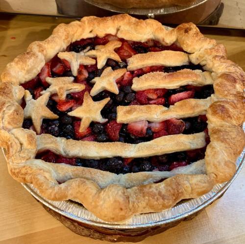 A patriotic pie with a star and stripe crust, filled with mixed berries, on a wooden surface.