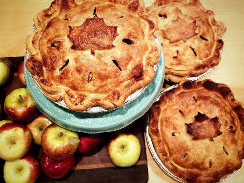 Three golden-brown apple pies with decorative crusts, surrounded by fresh red and green apples on a wooden surface.
