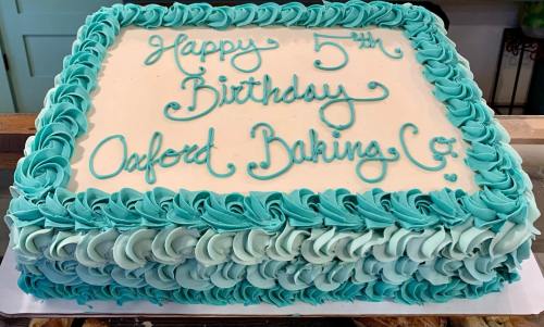 A rectangular birthday cake with turquoise frosting, reading "Happy 5th Birthday Oxford Baking Co." in elegant script.