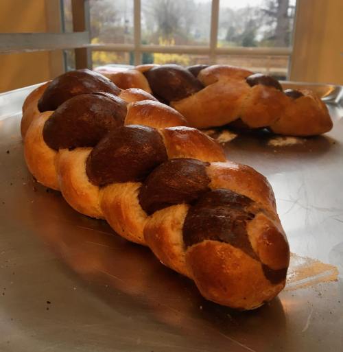A freshly baked braided bread with a golden crust and dark brown accents, resting on a silver tray.