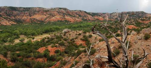 A scenic view of rugged, colorful cliffs and green vegetation in a canyon landscape under a cloudy sky.