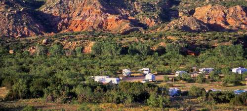 A scenic campsite surrounded by lush greenery and colorful rocky hills in the background.