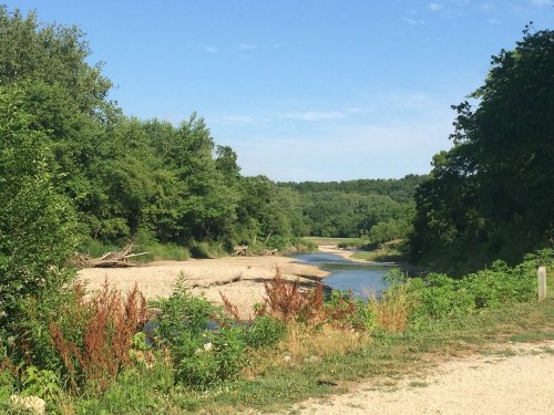 A serene river winding through lush greenery and sandy banks under a clear blue sky.