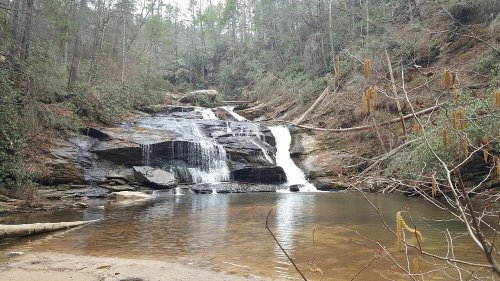 A serene waterfall cascades over rocks into a calm pool, surrounded by lush greenery and trees.