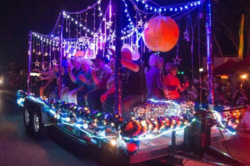 A brightly lit parade float decorated with lights and stars, featuring people sitting and celebrating.