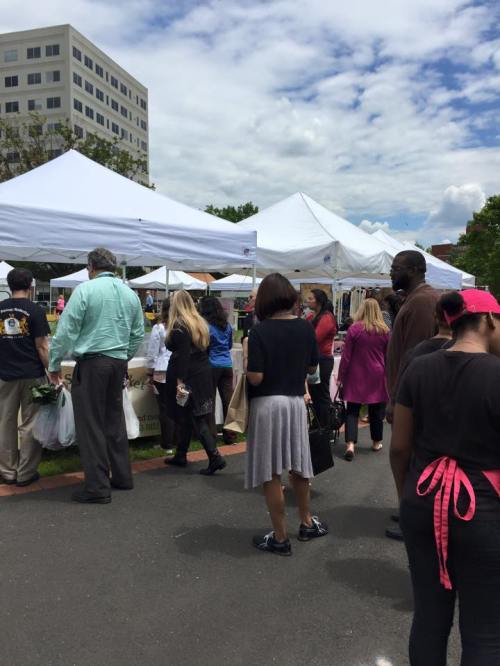 A busy outdoor market scene with people browsing under white tents on a cloudy day.