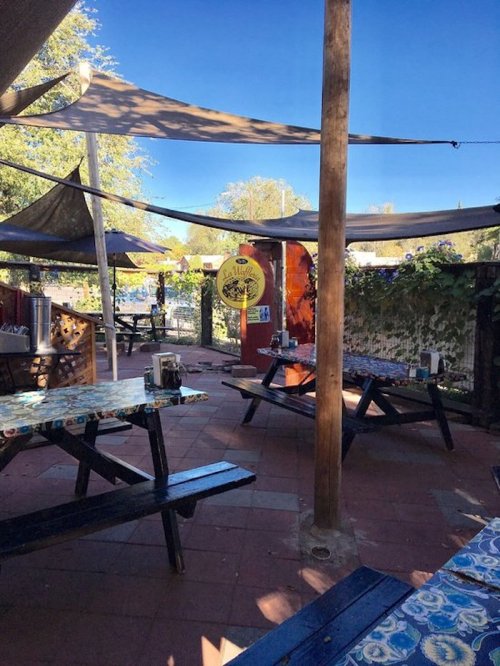 Outdoor dining area with shaded tables, colorful decor, and a view of greenery under a clear blue sky.