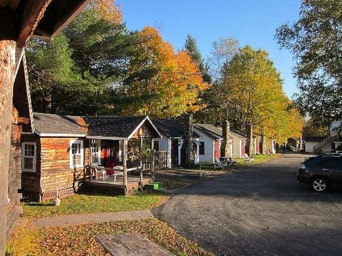 A row of quaint cabins lined along a tree-lined street, with vibrant autumn foliage in the background.