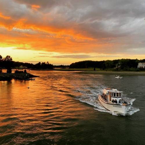 A boat glides through a river at sunset, with vibrant orange and purple clouds reflecting on the water.