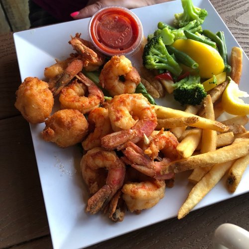 A plate of fried shrimp, hush puppies, French fries, and a side of mixed vegetables with a small cup of dipping sauce.