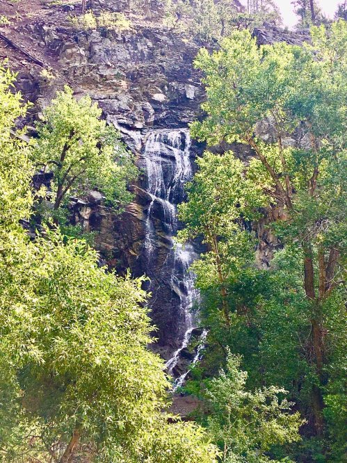 A serene waterfall cascading down rocky cliffs, surrounded by lush green trees and foliage.