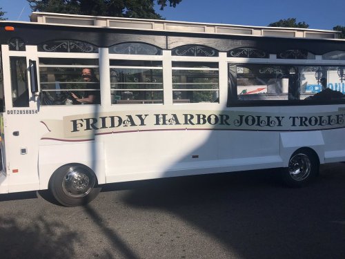 A white trolley bus with "Friday Harbor Jolly Trolley" written on the side, parked on a street.
