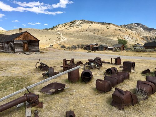 Abandoned buildings and rusted machinery scattered across a dry landscape with mountains in the background.