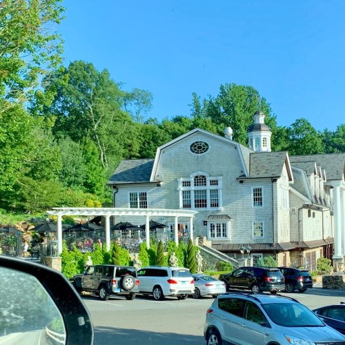 A large, elegant building surrounded by greenery, with parked cars in the foreground and a clear blue sky above.