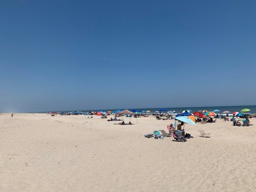 A sunny beach scene with colorful umbrellas and people relaxing on the sand near the ocean.