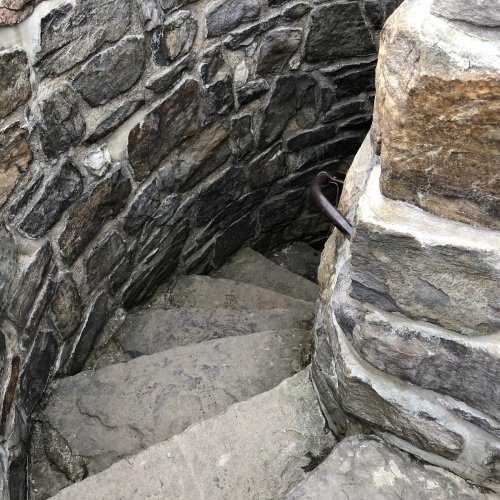 Stone spiral staircase descending into a dimly lit, circular stone structure.