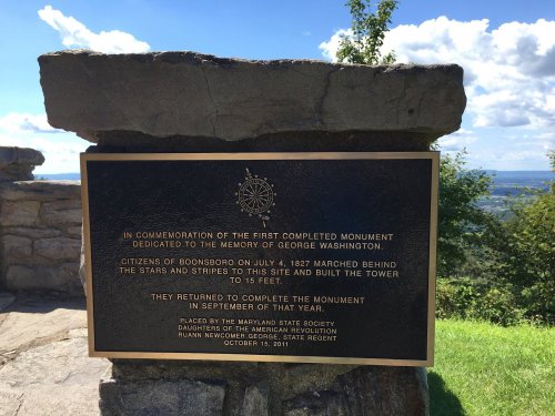 Plaque commemorating the first completed monument dedicated to George Washington, with a scenic view in the background.