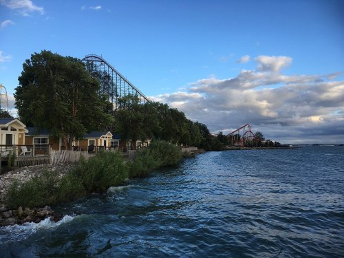 A scenic view of a lake with roller coasters in the background and trees lining the shore.