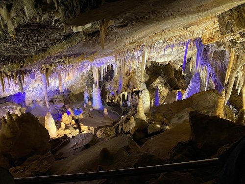 A stunning cave interior with stalactites and stalagmites illuminated by colorful lights.