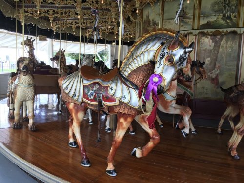 A beautifully crafted carousel horse with ornate details, surrounded by other carousel animals in a vintage setting.