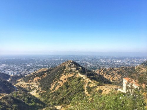 A panoramic view of a cityscape from a hillside, with clear blue skies and distant mountains in the background.