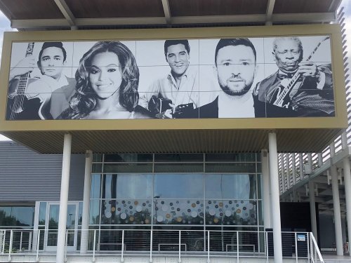 A building facade featuring large portraits of various musicians, including a woman with wavy hair and several men with instruments.