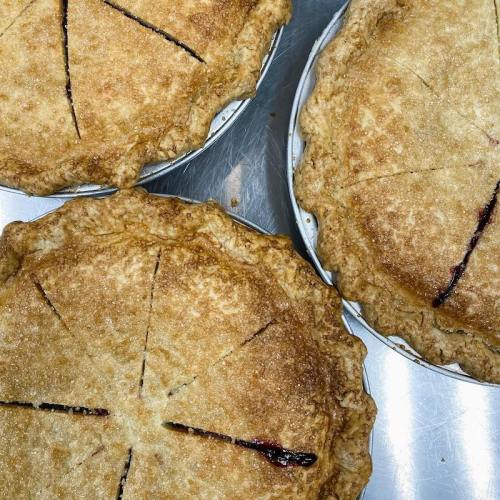 Three freshly baked pies with golden crusts, each sliced into wedges, resting on a silver surface.