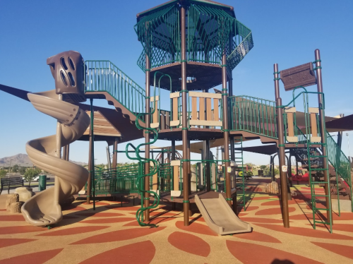 Colorful playground structure with slides, climbing features, and a tower under a clear blue sky.