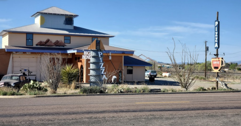 A pizza restaurant with a colorful sign, surrounded by desert landscape and a clear blue sky.