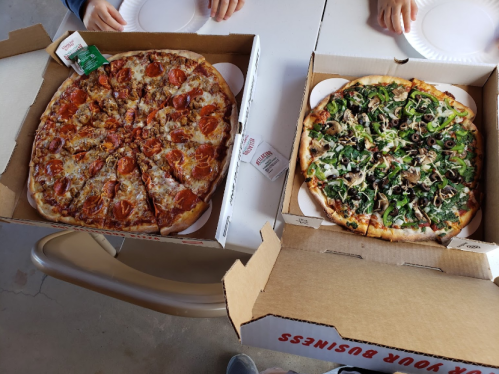 Two pizza boxes open on a table: one with pepperoni pizza and the other with a veggie pizza topped with mushrooms and olives.