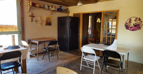 A rustic interior with a kitchen area, tables, chairs, and decorative items on the walls.