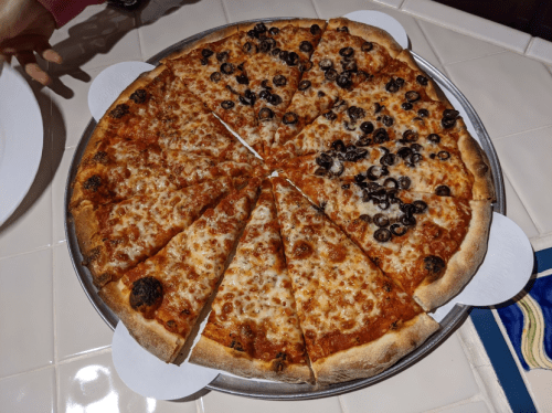 A large pizza on a round tray, half topped with olives and half plain cheese, cut into equal slices.