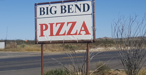 Sign for "Big Bend Pizza" along a roadside, with a clear blue sky and sparse vegetation in the background.