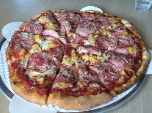 A pizza topped with ham, pineapple, cheese, and herbs, sliced into eight pieces on a wooden table.