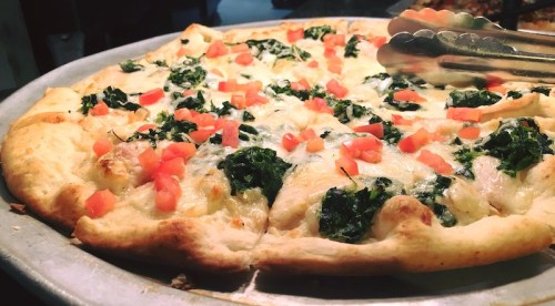 A freshly baked pizza topped with spinach, cheese, and diced tomatoes on a silver serving tray.