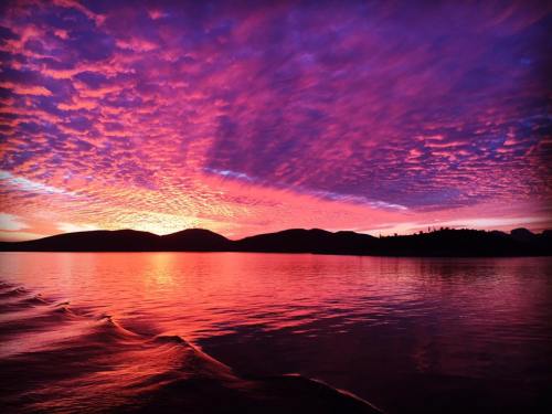 Vibrant sunset over a calm lake, with colorful clouds reflecting on the water and silhouetted mountains in the background.