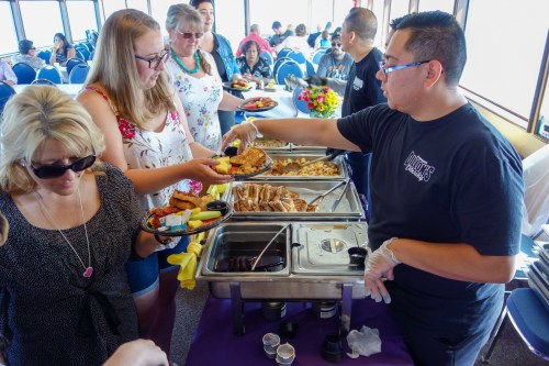 A buffet scene with people serving and enjoying food on a boat, featuring a variety of dishes and a festive atmosphere.