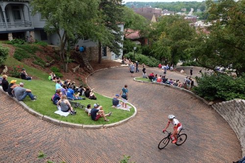 A cyclist rides down a winding, brick road while spectators watch from the grassy hillside and surrounding areas.