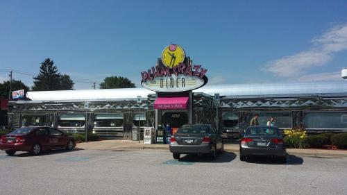 A shiny diner with a colorful sign, surrounded by parked cars and greenery under a clear blue sky.