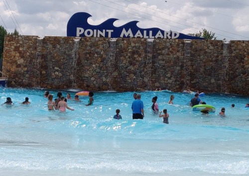 A crowded water park wave pool with people enjoying the water and a stone wall in the background.