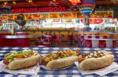 Three gourmet hot dogs with various toppings on a checkered tablecloth, with a vibrant restaurant background.