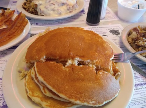 A plate of fluffy pancakes with a fork, surrounded by other dishes on a table.